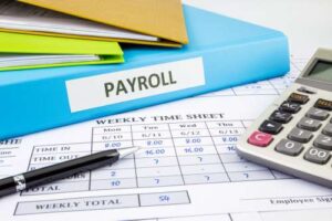 Payroll service Files on a desk saying payroll with a timesheet 